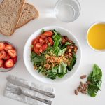 Top view of a healthy salad and fresh ingredients with bread and juice on a white surface.